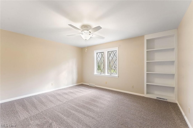 carpeted spare room with built in shelves and ceiling fan