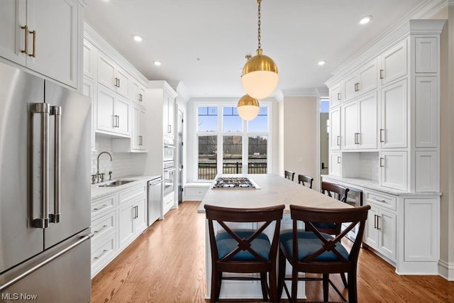 kitchen featuring decorative light fixtures, appliances with stainless steel finishes, light hardwood / wood-style floors, white cabinets, and sink