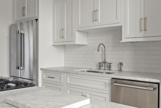 kitchen with sink, white cabinets, appliances with stainless steel finishes, backsplash, and light stone countertops