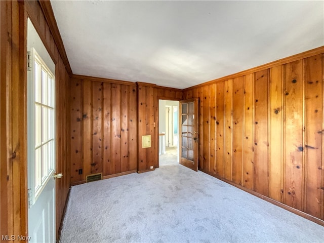 spare room featuring wood walls, crown molding, and light colored carpet