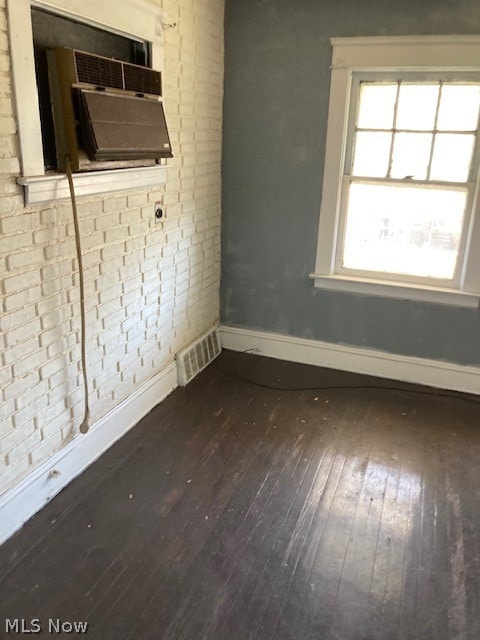 empty room featuring brick wall and dark wood-type flooring