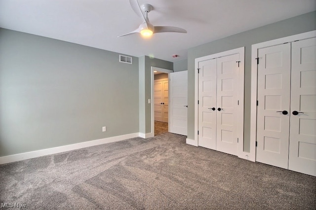 unfurnished bedroom with dark colored carpet, ceiling fan, and multiple closets