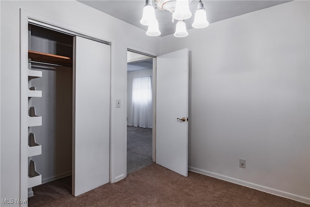 unfurnished bedroom featuring dark colored carpet, a closet, and a chandelier