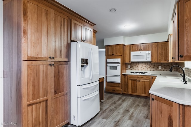 kitchen featuring backsplash, light wood-type flooring, white appliances, and sink