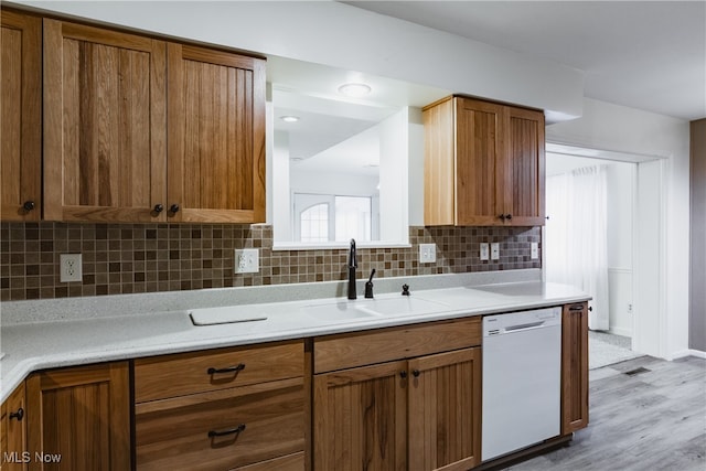 kitchen with light wood-type flooring, dishwasher, sink, and backsplash