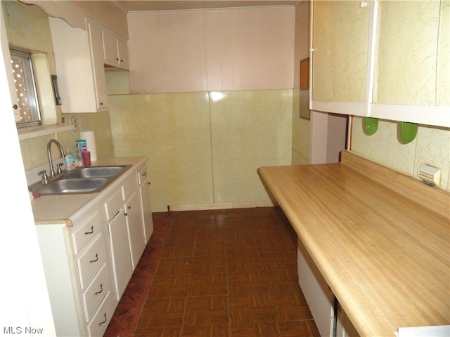 kitchen with sink, dark parquet flooring, and white cabinetry