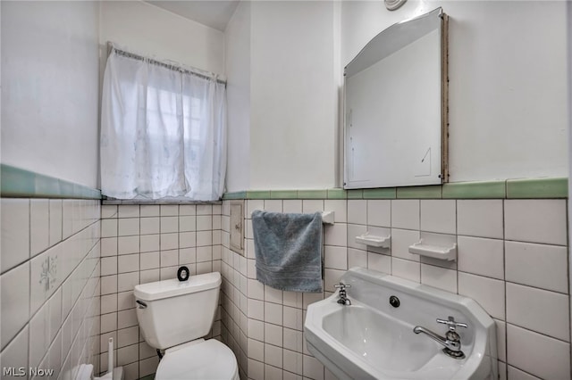 bathroom with toilet, sink, and tile walls