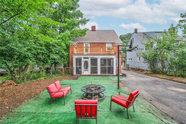 rear view of property with a balcony, an outdoor fire pit, a yard, and a sunroom