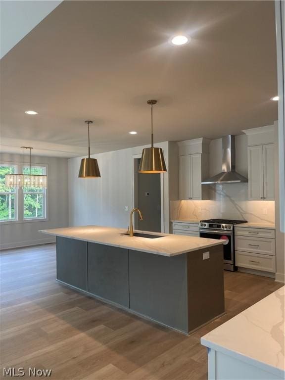 kitchen featuring sink, an island with sink, hanging light fixtures, gas stove, and wall chimney range hood