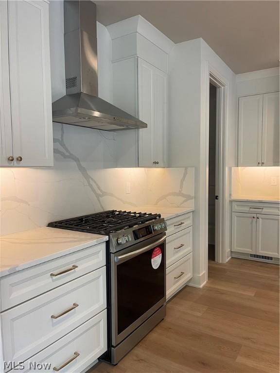 kitchen with gas stove, white cabinetry, light wood-type flooring, and wall chimney exhaust hood