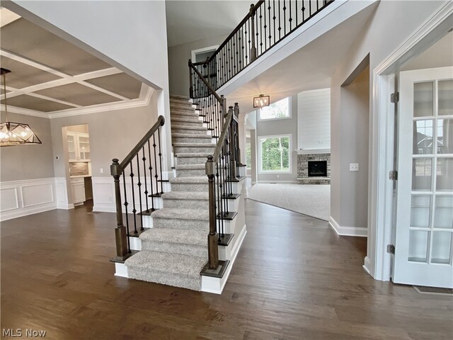 entrance foyer featuring coffered ceiling, dark hardwood / wood-style floors, a fireplace, and a chandelier