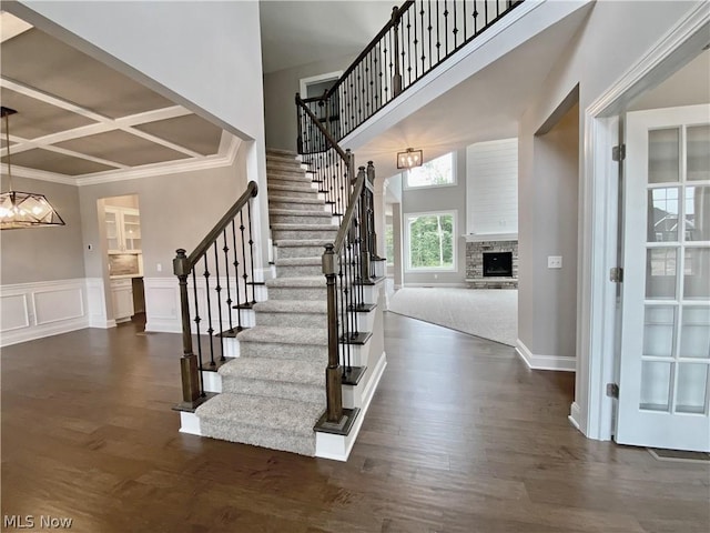 foyer featuring coffered ceiling, dark wood-type flooring, stairs, a high ceiling, and a fireplace