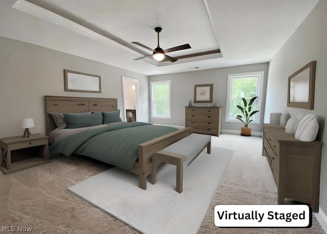 carpeted bedroom with a raised ceiling, multiple windows, ceiling fan, and ensuite bathroom