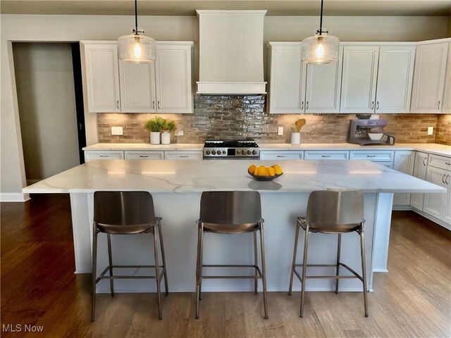 kitchen featuring a kitchen island, white cabinetry, premium range hood, and gas range