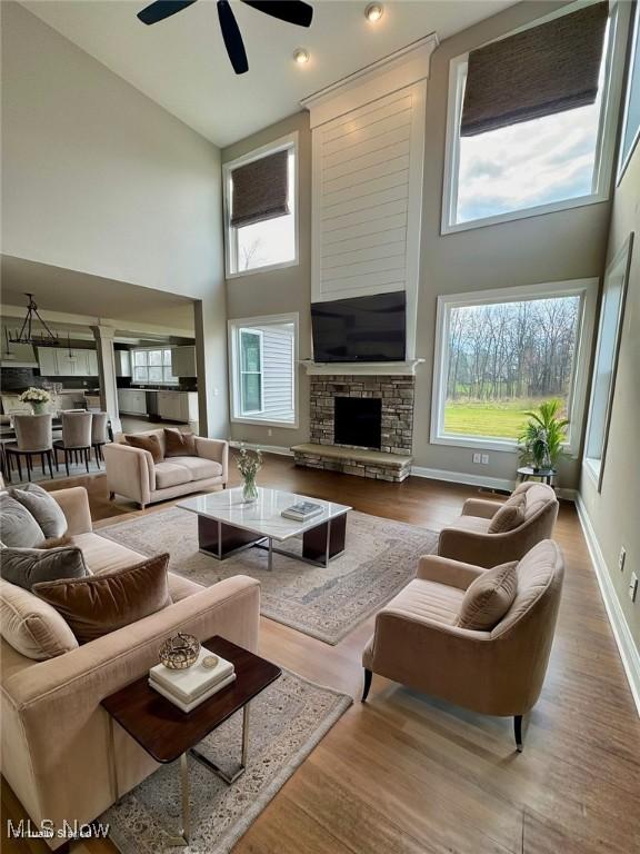 living room with ceiling fan, a stone fireplace, wood-type flooring, and a high ceiling