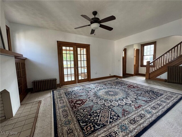 unfurnished living room featuring french doors, ceiling fan, radiator, and light carpet