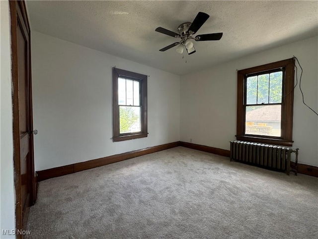 carpeted spare room featuring a healthy amount of sunlight, radiator heating unit, and a textured ceiling