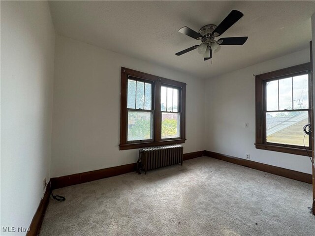 spare room with radiator heating unit, light colored carpet, and ceiling fan