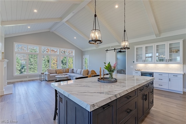 kitchen with backsplash, a barn door, light hardwood / wood-style flooring, light stone countertops, and white cabinets