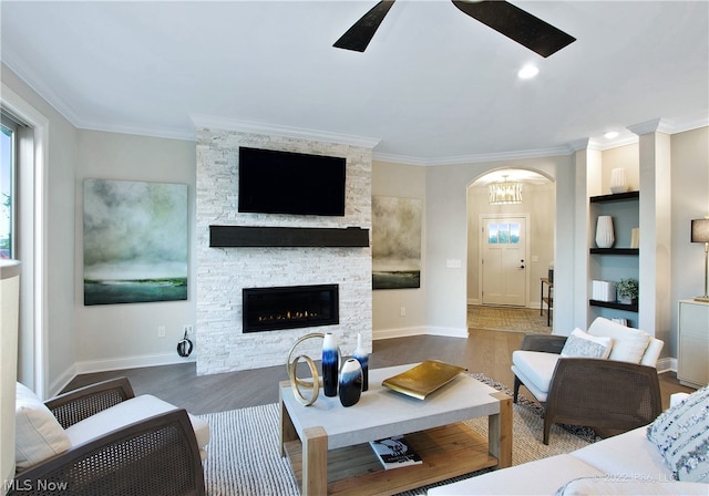 living room with crown molding, built in shelves, dark hardwood / wood-style flooring, ceiling fan, and a fireplace