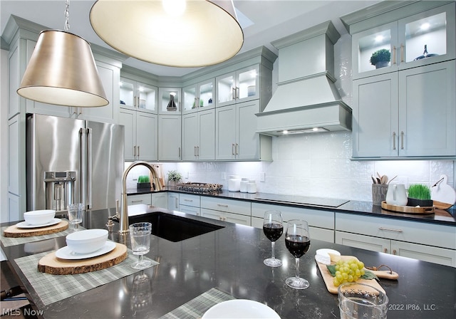 kitchen with black electric stovetop, premium range hood, hanging light fixtures, high end refrigerator, and backsplash