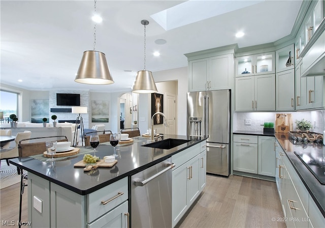 kitchen featuring hanging light fixtures, an island with sink, light wood-type flooring, sink, and appliances with stainless steel finishes