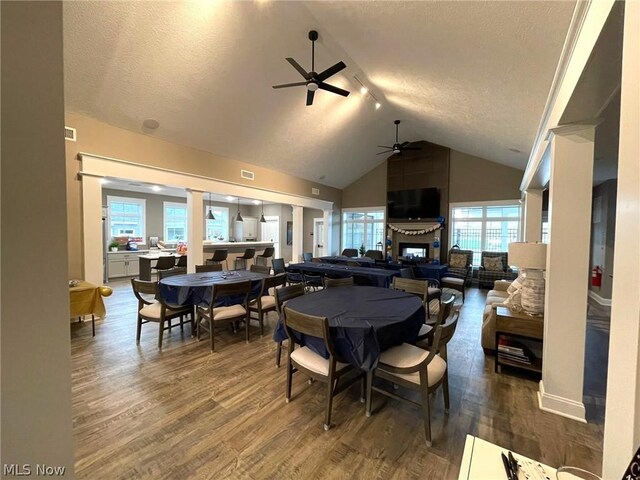 dining room featuring hardwood / wood-style floors, a fireplace, a textured ceiling, high vaulted ceiling, and ceiling fan