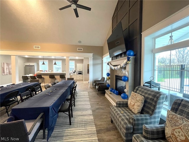 living room with high vaulted ceiling, a tiled fireplace, ceiling fan, and hardwood / wood-style flooring