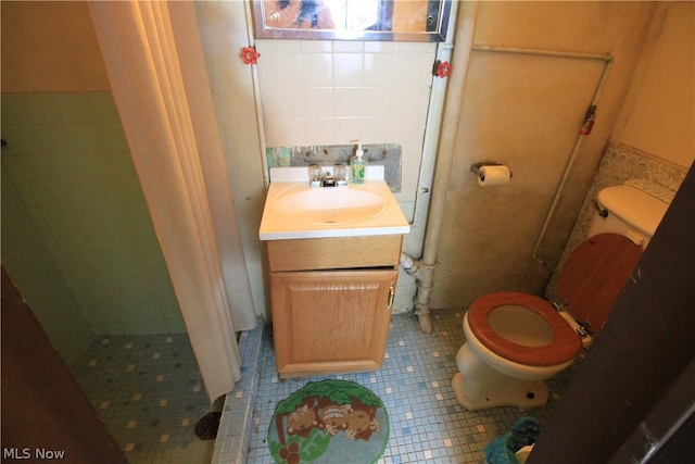 bathroom featuring a tile shower, toilet, tile patterned flooring, vanity, and tile walls