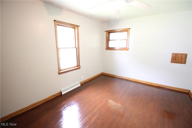 spare room with ceiling fan, a wealth of natural light, dark wood-type flooring, and a baseboard heating unit