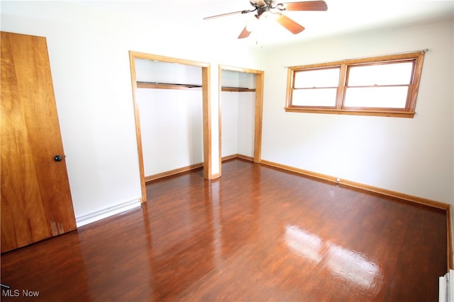 unfurnished bedroom featuring ceiling fan, two closets, and dark wood-type flooring