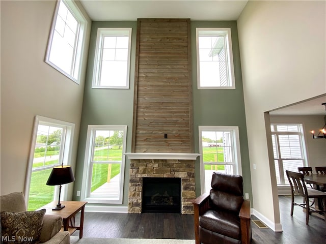 living room featuring dark wood-type flooring, a stone fireplace, an inviting chandelier, and a high ceiling