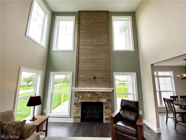 living room with a fireplace, a towering ceiling, dark wood-type flooring, a chandelier, and baseboards