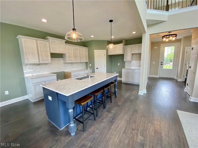 kitchen featuring a center island with sink, baseboards, white cabinets, dark wood-type flooring, and a sink