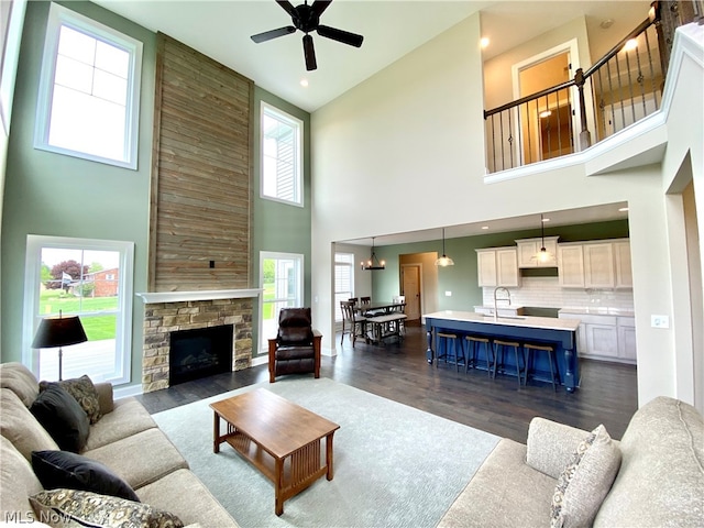 living room with dark hardwood / wood-style flooring, sink, a stone fireplace, and ceiling fan