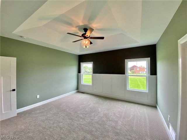 carpeted empty room with a raised ceiling, a ceiling fan, and baseboards