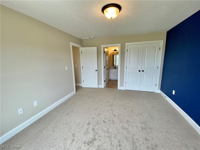 unfurnished bedroom with a closet, carpet flooring, baseboards, and ensuite bathroom