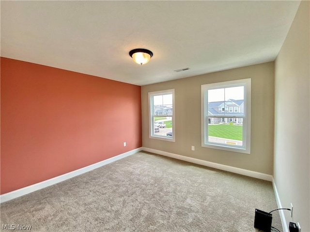 empty room with carpet flooring, visible vents, and baseboards