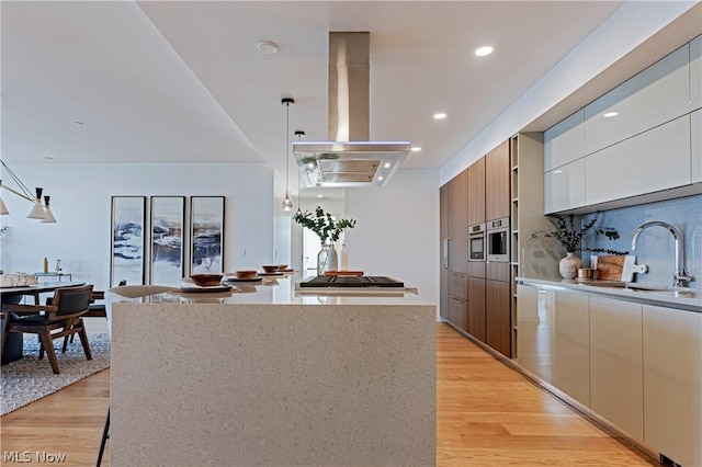 kitchen with pendant lighting, island range hood, light hardwood / wood-style floors, and sink