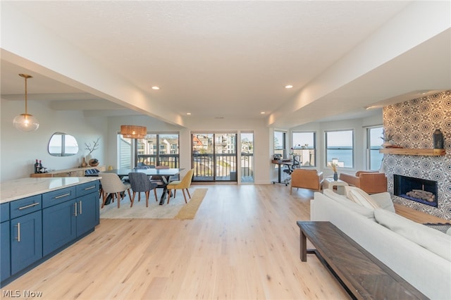 living room featuring a tiled fireplace, plenty of natural light, a water view, and light wood-type flooring