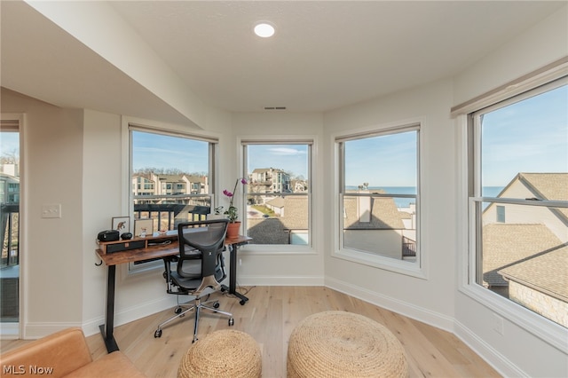 home office with a water view, a wealth of natural light, and light hardwood / wood-style floors