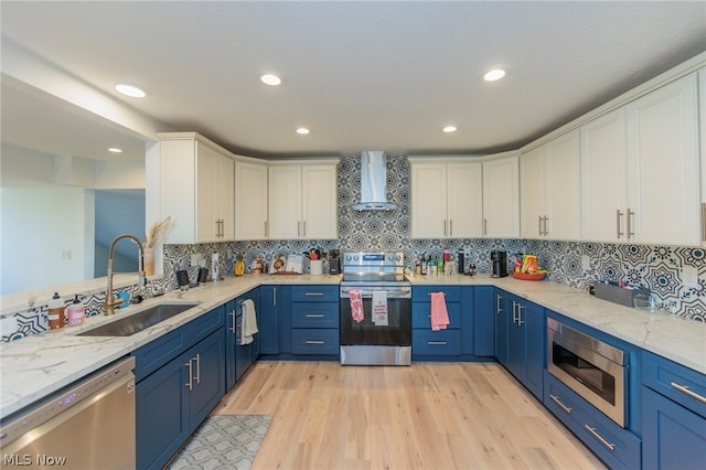 kitchen with light hardwood / wood-style flooring, stainless steel appliances, sink, white cabinetry, and wall chimney range hood