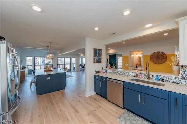 kitchen featuring light wood-type flooring, light stone counters, stainless steel appliances, sink, and blue cabinets