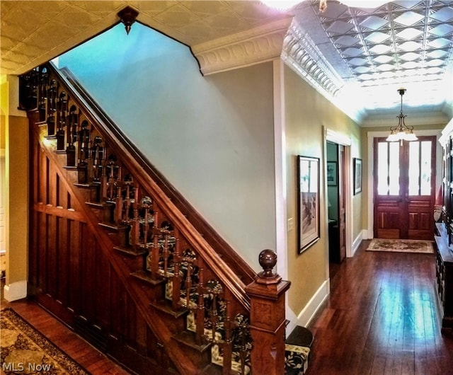 stairway with an inviting chandelier, ornamental molding, and dark hardwood / wood-style floors