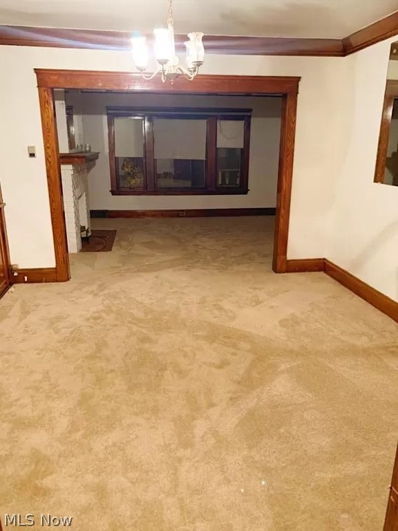 empty room featuring a chandelier, light colored carpet, and a fireplace