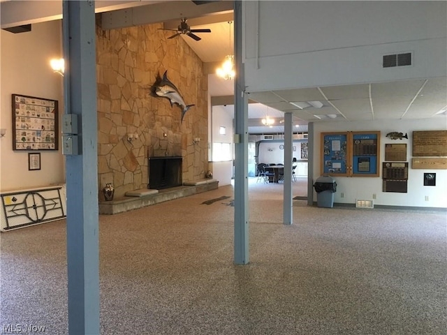 unfurnished living room featuring carpet floors, ceiling fan, a paneled ceiling, and a stone fireplace