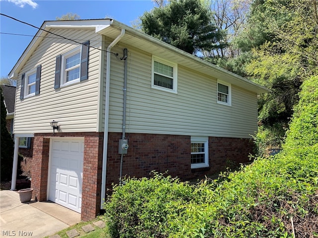 view of side of property with an attached garage, concrete driveway, and brick siding