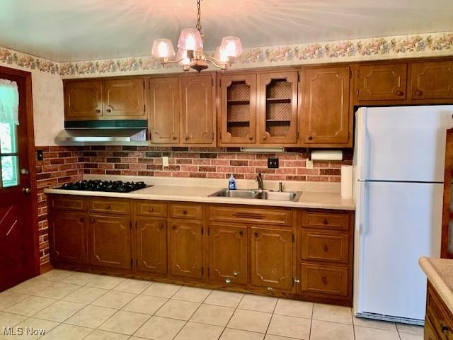 kitchen featuring black gas stovetop, a sink, light countertops, freestanding refrigerator, and range hood