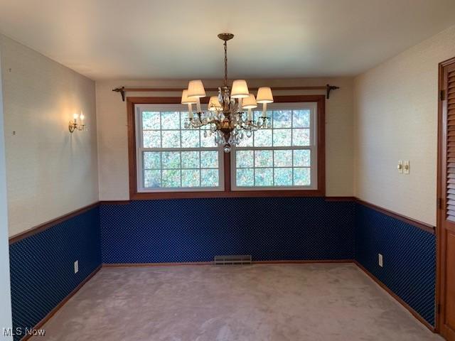 empty room featuring carpet, wainscoting, visible vents, and an inviting chandelier