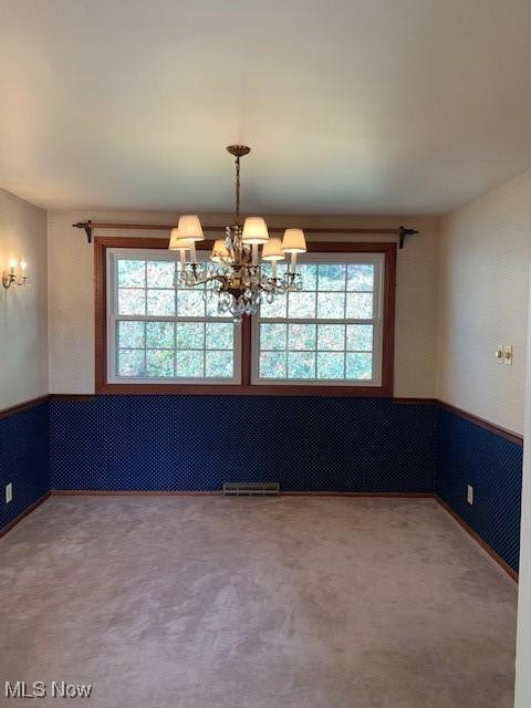 unfurnished dining area with a wealth of natural light, carpet, and a chandelier